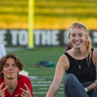 Two students stretching and sitting on the Football Field during a yoga session at sunset